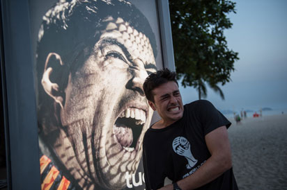 A tourist jokes in front of an advertisement with the portrait of Uruguay's forward Luis Suarez at Copacabana beach in Rio de Janeiro, Brazil, on June 26, 2014. Sportswear giant Adidas said Thursday it would stop using Luis Suarez, one of its key promotional stars, for World Cup adverts after his four-month ban from football activities for biting Italian Giorgio Chiellini. AFP PHOTO / YASUYOSHI CHIBA