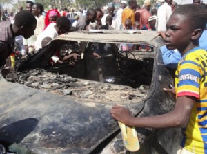 Residents look at a burnt car outside the central mosque in northern Nigeria's largest city of Kano on Novemer 29, 2014, a day after twin suicide blasts hit the mosque during weekly Friday prayers. At least 120 people were killed and 270 others wounded when two suicide bombers blew themselves up and gunmen opened fire during weekly prayers at the mosque, a week after the emir of Kano, Muhammad Sanusi II, of one of Nigeria's top Islamic leaders called on northerners to defend themselves against Boko Haram Islamists that have been carrying out deadly attacks and seizure of territory in the northeast. AFP PHOTO