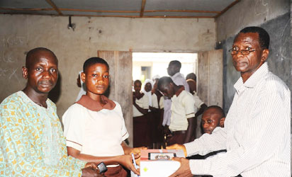 The Principal  of Kuta Community  High School,  Mr Asifat musibau (right),   giving  a Tablet of knowledge  (OPON IMO),  to a student, Oyelude Ayomide. With   them is her father,   Mr Oyedeji  Samson (left), during the distribution  of   Tablet of knowledge by the State Government to students of Kuta  Community  High   school, Kuta,  State of Osun 