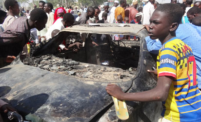 Residents look at a burnt car outside the central mosque in northern Nigeria's largest city of Kano on Novemer 29, 2014, a day after twin suicide blasts hit the mosque during weekly Friday prayers. At least 120 people were killed and 270 others wounded when two suicide bombers blew themselves up and gunmen opened fire during weekly prayers at the mosque, a week after the emir of Kano, Muhammad Sanusi II, of one of Nigeria's top Islamic leaders called on northerners to defend themselves against Boko Haram Islamists that have been carrying out deadly attacks and seizure of territory in the northeast. AFP PHOTO