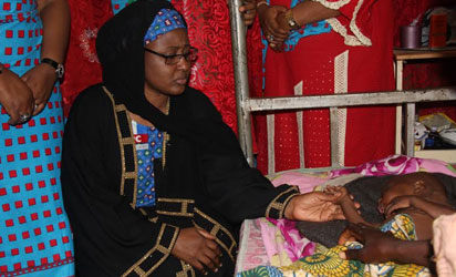Hajia Aisha Buhari holding the hand of a sick child at one of the IDP camps in Adamawa State 
