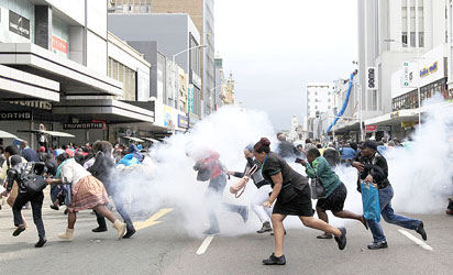 People take cover from a stun grenade and tear gas after a skirmish between locals and foreign nationals as thousands of people take part in the "peace march" against xenophobia in Durban, South Africa, on April 16, 2015. South African President Jacob Zuma on April 16 appealed for the end of attacks on immigrants as a wave of violence that has left at least six people dead threatened to spread across the country. In the past two weeks, shops and homes owned by Somalis, Ethiopians, Malawians and other immigrants in Durban and surrounding townships have been targeted, forcing families to flee to camps protected by armed guards. AFP PHOTO